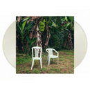 Two white chairs under a banana tree in a tropical setting